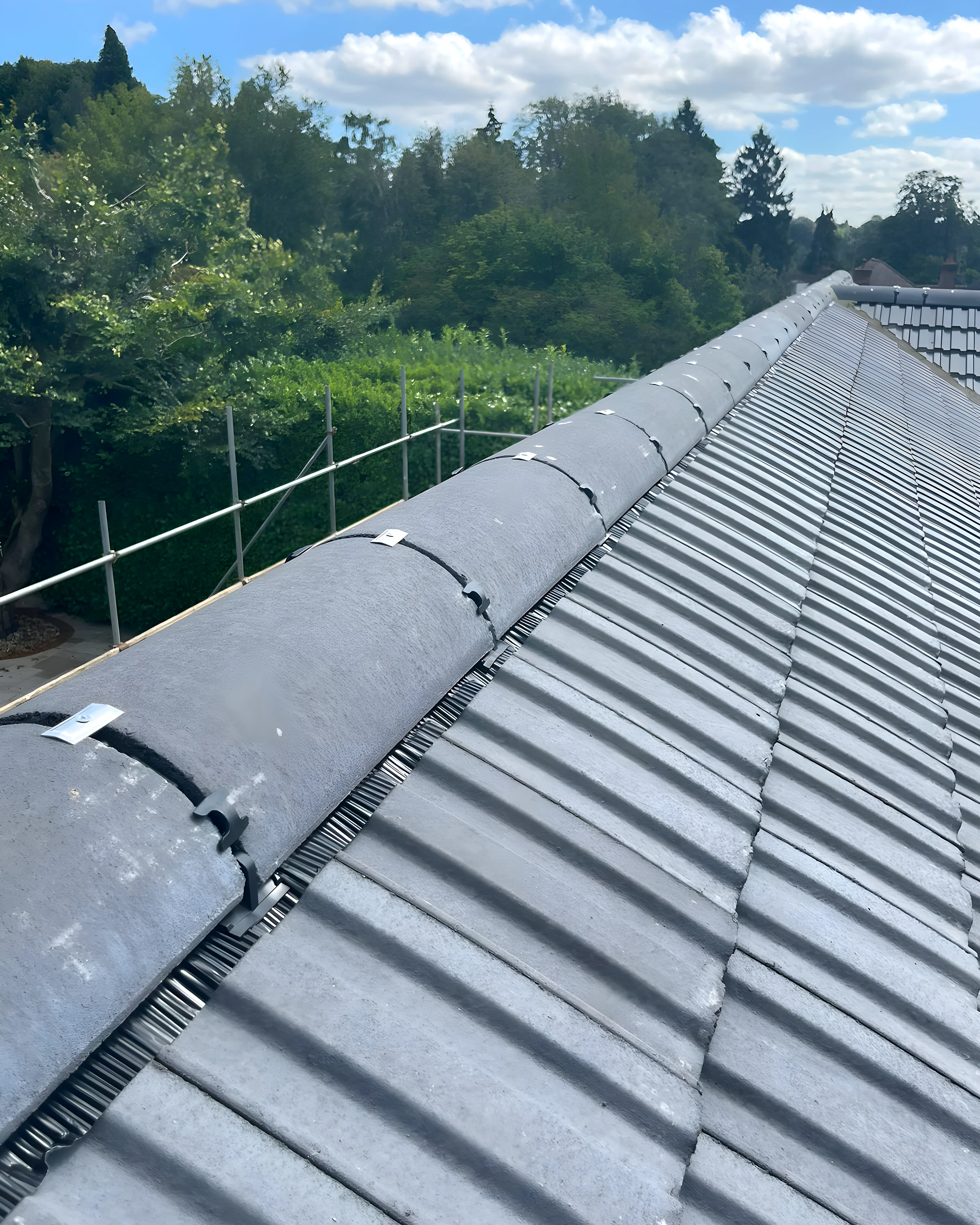 New ridge bedded along a grey tiled roof, photographed from the scaffold