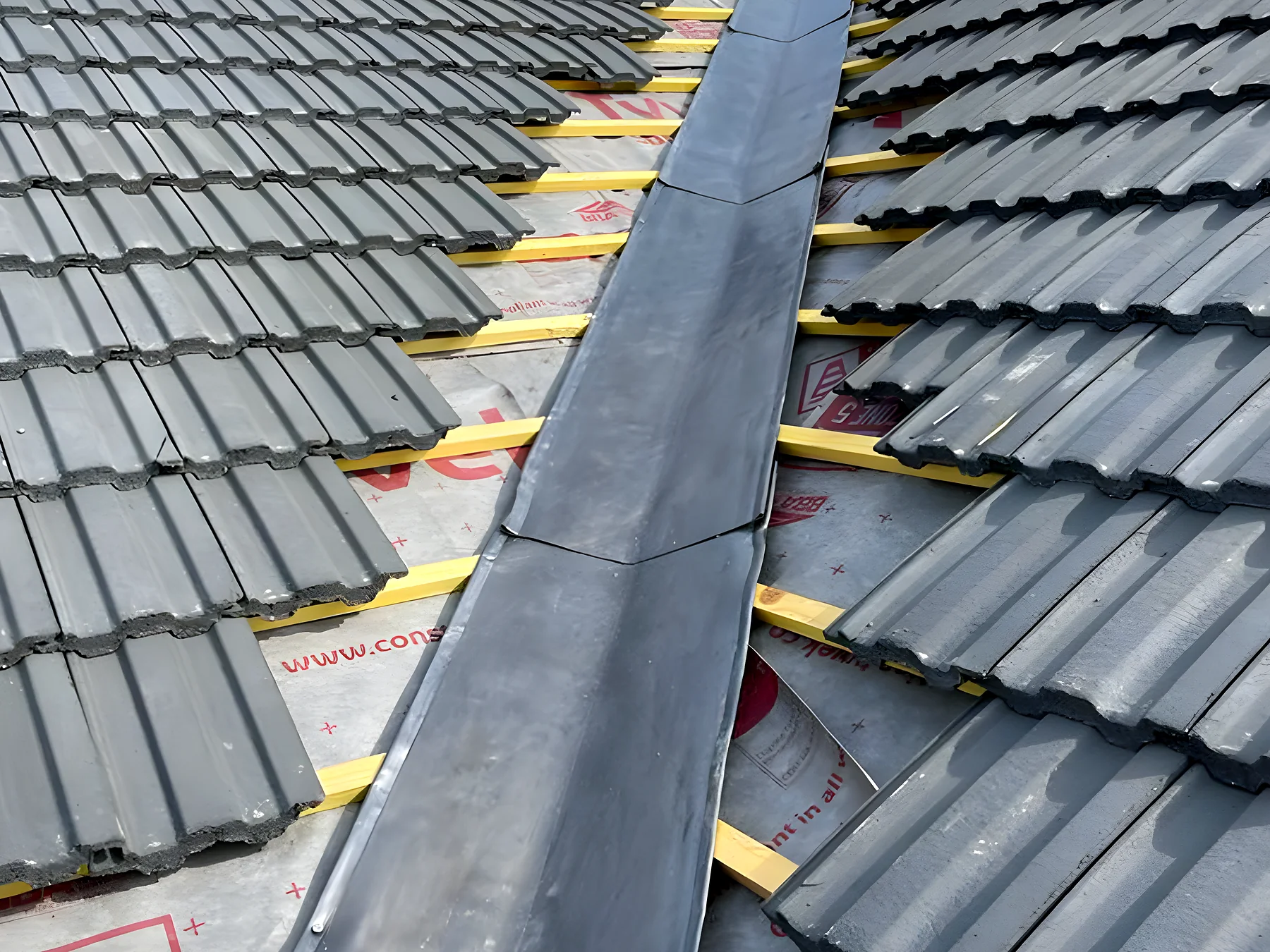 Freshly dressed lead valley set between two runs of grey roof tiles