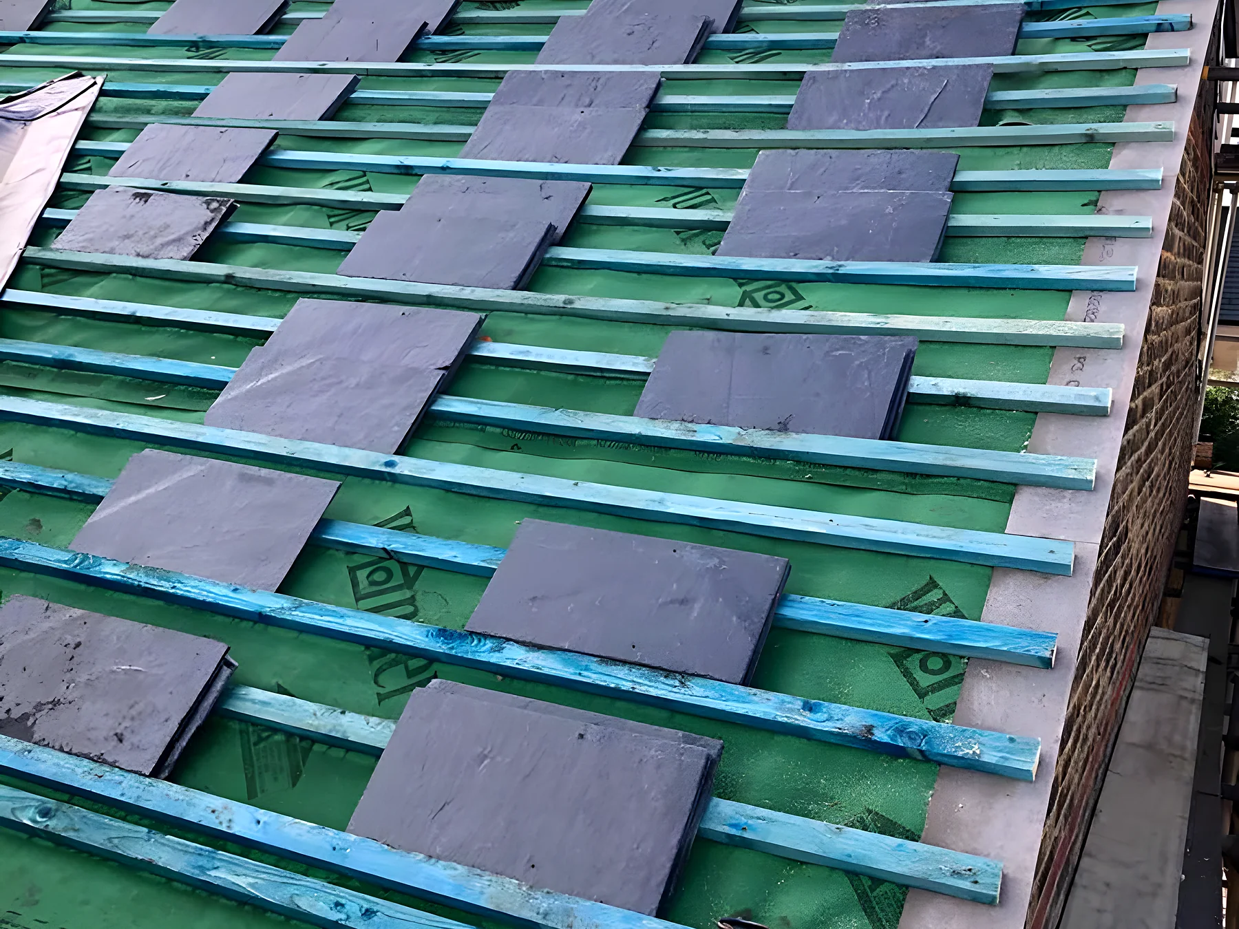 New battens and underlay across a stripped roof with slates being loaded out